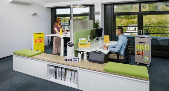 Eine Person sitzt am Arbeitsplatz während die Person gegenüber im stehen arbeitet