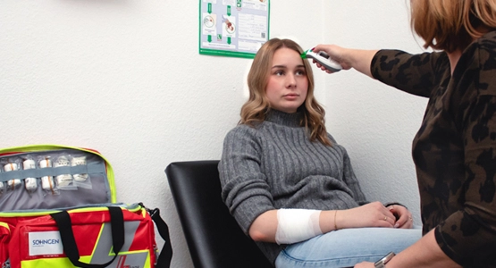 Eine junge Frau wird mit einem Thermometer an der Stirn untersucht.