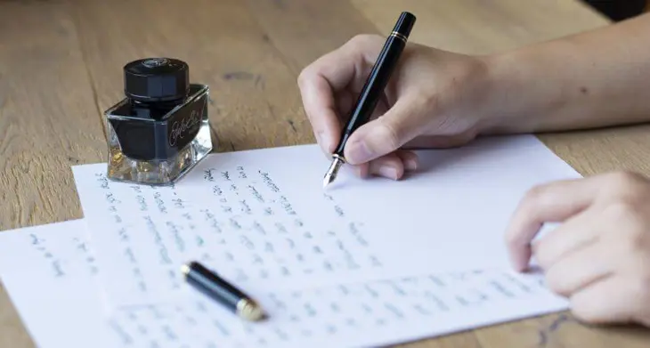 Eine Hand schreibt mit Füllhalter und Tinte einen handschriftlichen Brief.