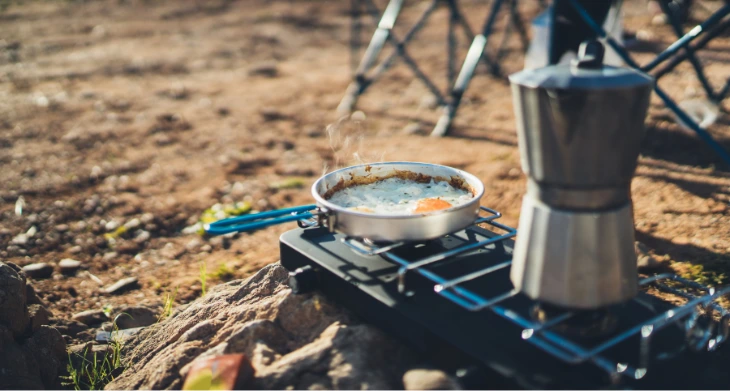 Campingkocher am See mit Spiegeleier in Pfanne und Espressokocher.