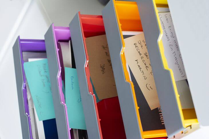 Eine Schubladenbox von Durable mit 5 bunten Schubbladen wurde von oben fotografiert. Die Schubbladen sind geöffnet und darin sieht man verschiedene, beschriebene Haftnotizen.