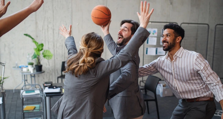 Drei Büromitarbeitende spielen Basketball im Büro.