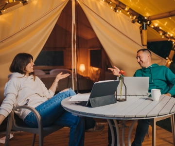 Zwei Personen arbeiten entspannt mit Laptops vor Zelt im Abendlicht.