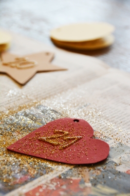 Auf einem Tisch liegt ein gebastelter Adventskalender Anhänger in Herzform mit der Nummer 21. Darauf ist Glitzerstaub verteilt.