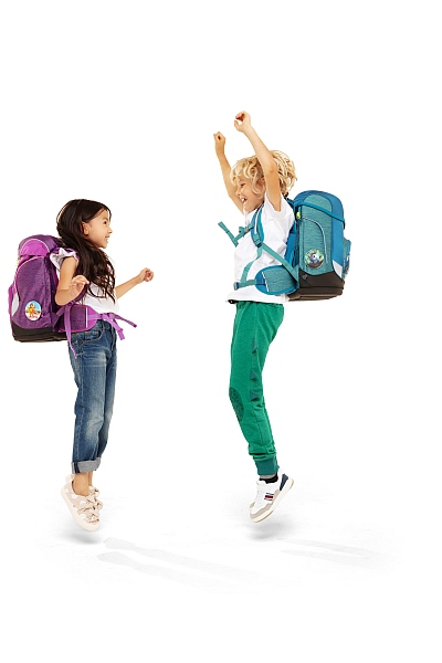 Zwei Kinder mit ergobag Rucksäcken freuen sich und hüpfen nebeneinander in die Luft.