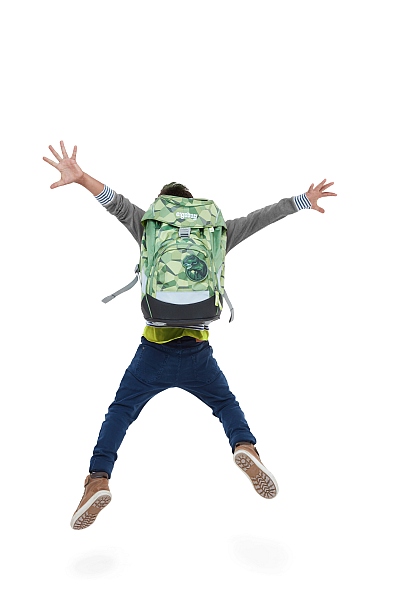 Junge mit grünem ergobag Rucksack springt jubelnd mit ausgebreiteten Armen in die Luft.