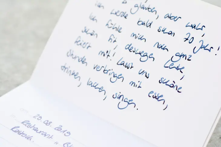 Eine aufgeklappte Karte, welche eine Einladung in Gedichtform zeigt, wurde mit Füller geschrieben.