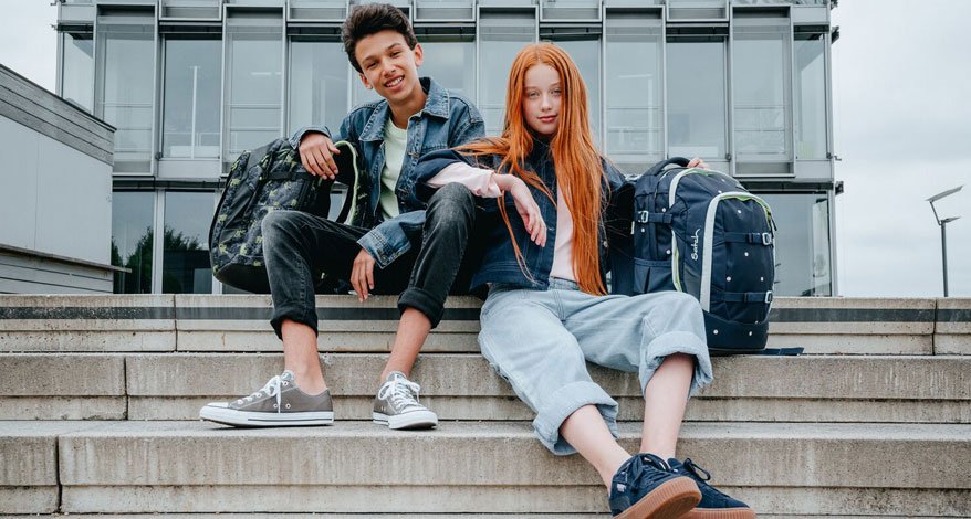 Zwei Jugendliche sitzen mit ihren Rucksäcken der Marke satch auf einer Treppe.
