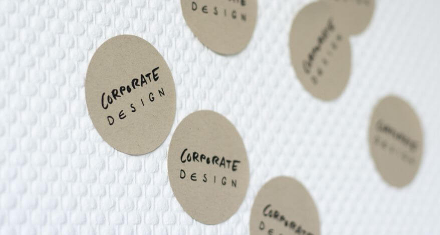 Runde Aufkleber mit „Corporate Design“ auf strukturierter Wand