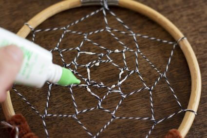 Nahaufnahme eines selbstgebastelten Traumfängers. Auf das Netz wird flüssiger Klebstoff aufgetragen.