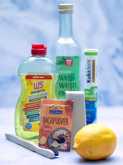 Verschiedene Hausmittel, mit den man Flecken aus (Arbeits-)Kleidung entfernen kann, sind zu sehen: Spülmittel, Essig, Backpulver, Zitronen, Gallseife, Zahnreinigertabs und eine Zahnbürste. Foto: Johanna Rundel