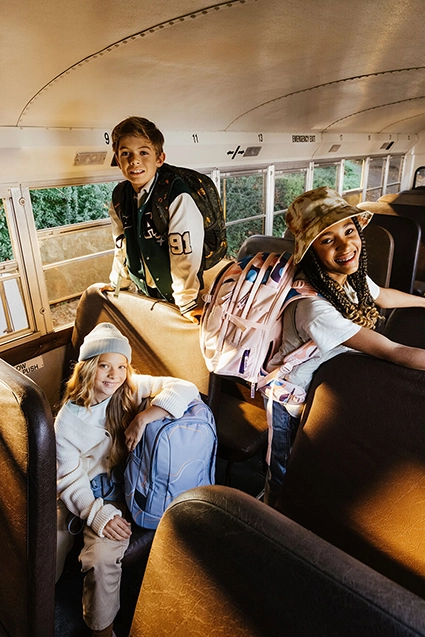 Eine Gruppe Jugendliche sitzen lässig mit ihren Schulrucksäcken von satch in einem gelben Schulbus.