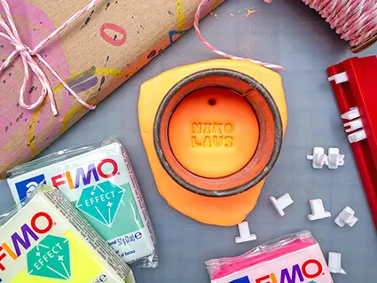 Aus Fimo von STAEDTLER in neonorange wurde ein runder Geschenkanhänger ausgestochen. In der Mitte wurde das Wort „Nikolaus“ eingeprägt. Foto: Johanna Rundel