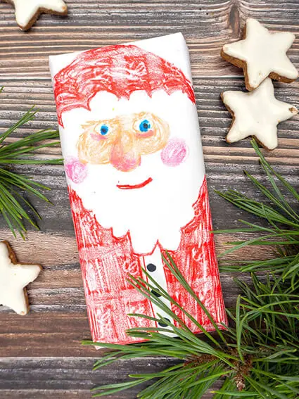 Auf einer rustikalen Holzplatte liegt eine weihnachtlich verpackte und mit Stiften von STAEDTLER als Nikolaus bemalte Schokoladentafel. Foto: Johanna Rundel