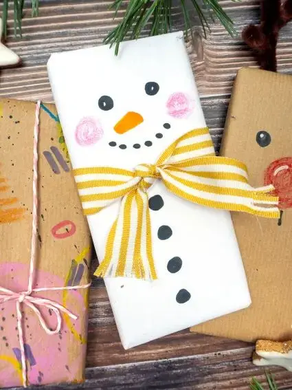 Auf einer rustikalen Holzplatte liegt eine weihnachtlich verpackte und mit Stiften von STAEDTLER als Schneemann bemalte Schokoladentafel. Foto: Johanna Rundel