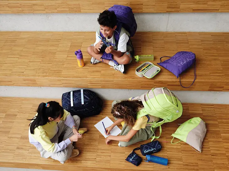 Drei Schüler sitzen umgeben von Ihren Schulsachen der Marke satch auf einer Treppe und lernen.