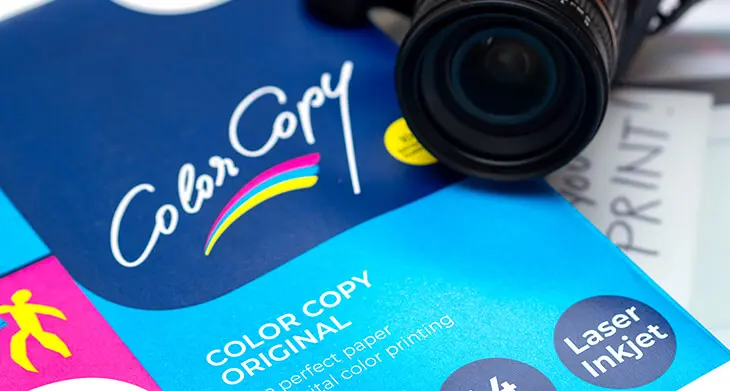 Auf einer Packung Kopierpapier mit 300 g/m² liegt eine schwarze Fotokamera. Darunter ist eine Farbkopie zu sehen. Foto: Johanna Rundel