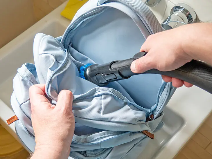 Jemand saugt mit einem Staubsauger das Innere eines hellblauen Schulrucksacks von satch aus. Foto: Johanna Rundel