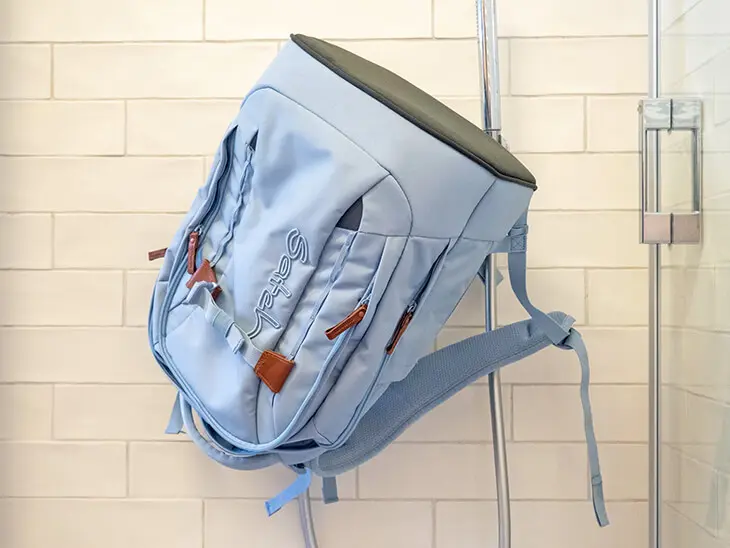 Ein hellblauer Schulrucksack von satch hängt kopfüber an der Duscharmatur in einer hellbeigen gefliesten Duschkabine. Foto: Johanna Rundel