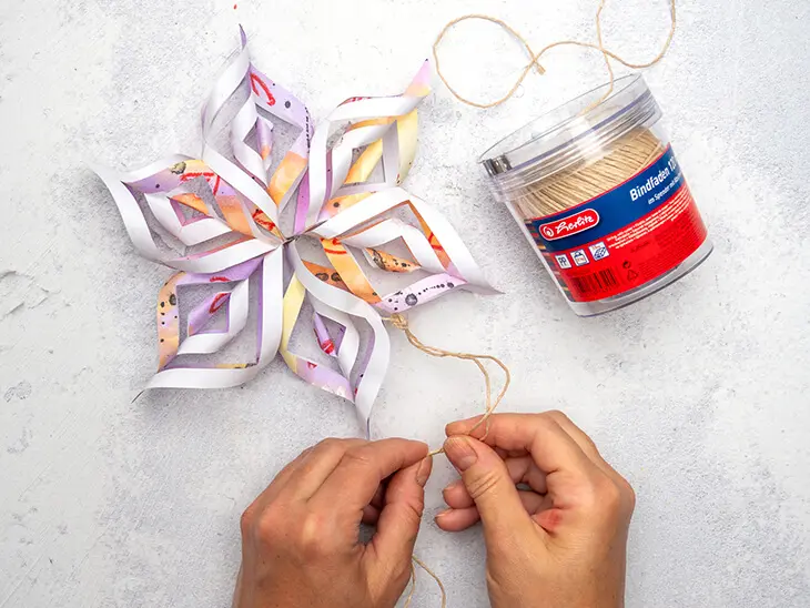 Jemand befestigt eine Kordel von herlitz an einem bunten Papierstern. Foto: Johanna Rundel