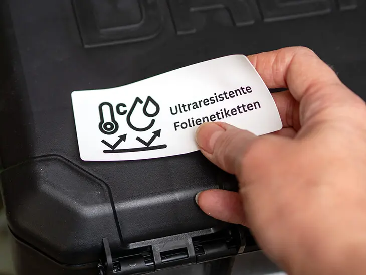 Jemand klebt ein ultraresistentes Folienetikett von Avery Zweckform auf einen Werkzeugkoffer. Foto: Johanna Rundel