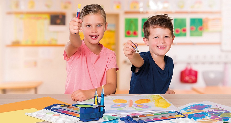 Zwei Kinder malen fröhlich mit Wasserfarben in einem bunten Klassenraum.