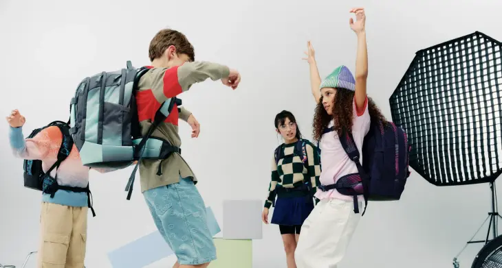 Mehrere Kinder mit satch Rucksäcken auf dem Rücken springen vor einem Scheinwerfer eines Filmsets.