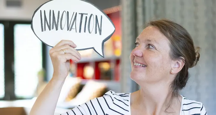 Eine Frau hält eine Sprechblase in die Luft, auf der das Wort „Innovation“ steht.