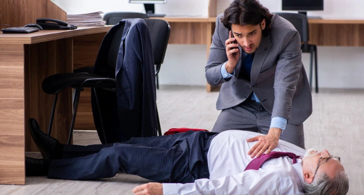Mann im Anzug leistet Erste Hilfe und ruft Notruf für bewusstlosen Kollegen.