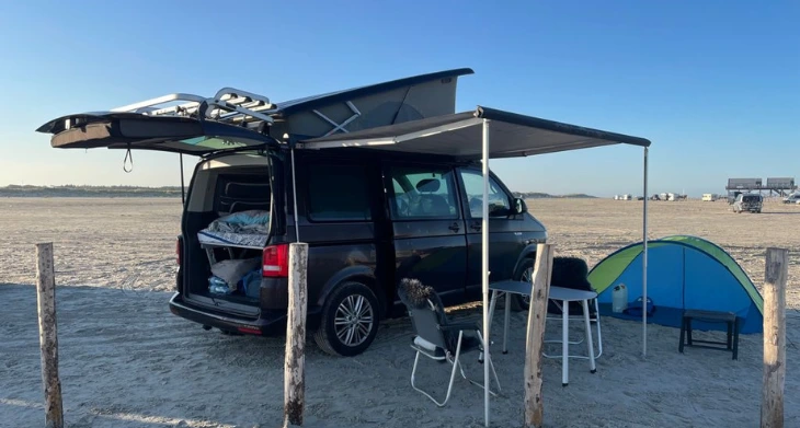 Camper mit Markise und Zelt am Strand bei sonnigem Wetter.