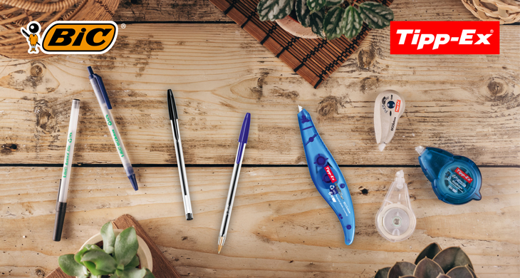 Nachhaltige BIC Kugelschreiber und Tipp-Ex Korrekturroller auf einem Schreibtisch aus Holz mit Pflanzen. Markenlogos von BIC und Tipp-Ex in den Ecken.