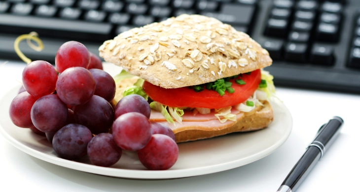 Vollkornbrötchen und Trauben auf Teller vor Computertastatur am Schreibtisch