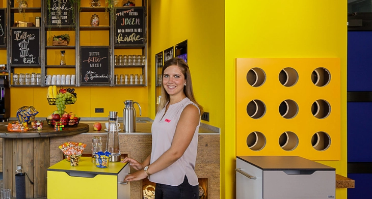 Zwei Kollegen in moderner Büroküche mit Snacks und Getränken.