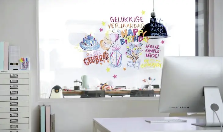 In einem Büro ist die Fensterscheibe mit bunten Geburtstagsgrüßen geschmückt, Auf einem Schrank daneben steht eine Stiftebox mit edding Glasmarkern.
