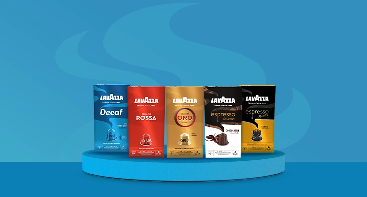 Fünf verschiedene Verpackungen mit Lavazza Kaffeekapseln stehen auf einem blauen Podest vor blauem Hintergrund.