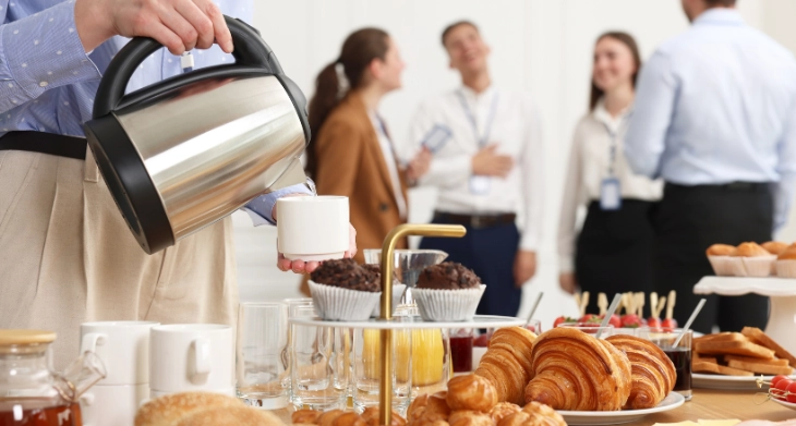 Person schenkt Kaffee bei Konferenz mit Gebäck ein.