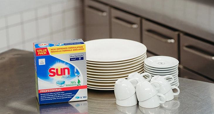 Eine Packung Sun Spülmaschinentabs steht neben strahlend sauberem Geschirr in einer Küche.