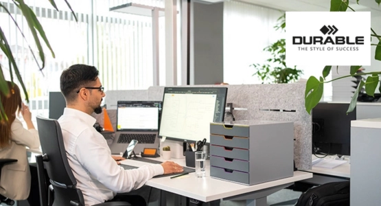 Ein Mann sitzt an einem Schreibtisch vor dem PC, neben im eine Schubladenbox von Durable.