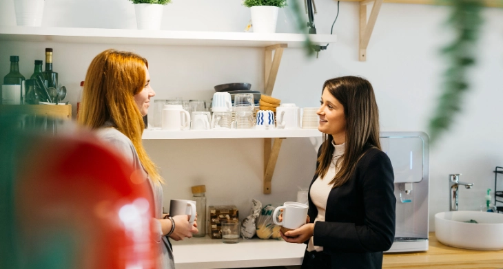 Zwei Kolleginnen plaudern bei Kaffee in gut ausgestatteter Büroküche.