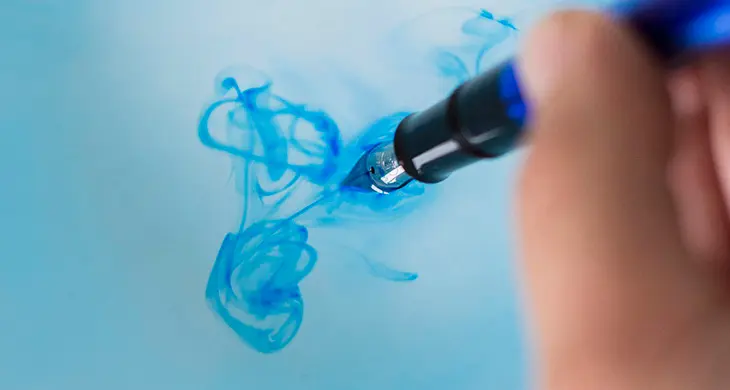 Ein Füller wird mit Wasser gereinigt, das mit Tinte gefärbt in eine Schale tropft.