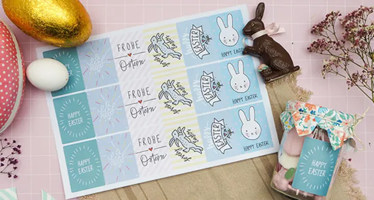 Auf einem rosa Untergrund liegt ein Etikettenbogen von Avery Zweckform. Die Aufkleber haben verschiedene Ostermotive. Rundherum liegt Osterdekoration verstreut. Foto: Johanna Rundel