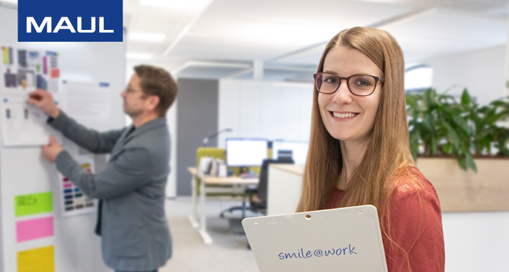 Frau mit MAUL-Klemmbrett mit Aufschrift „smile@work“ in modernem Büro.