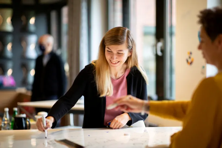 Zwei Frauen stehen sich an einem Tisch gegenüber, an dem sie arbeiten.