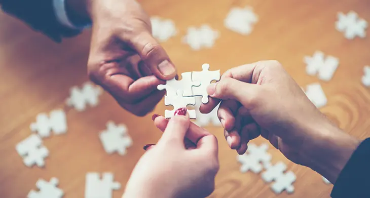 Drei Hände fügen Puzzleteile zusammen.