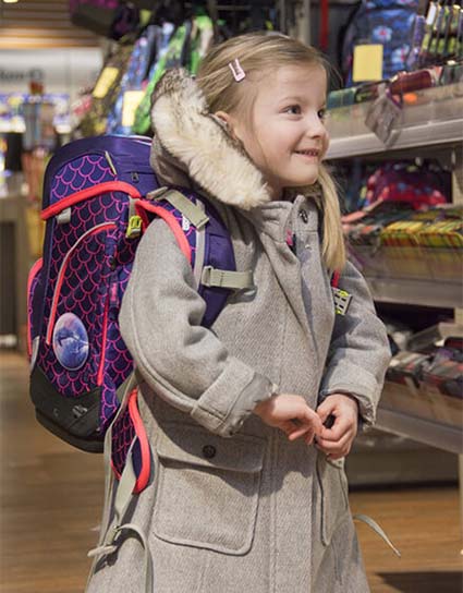 Eine zukünftige Erstklässlerin steht nach einer Ranzen Beratung stolz mit ihrem neuen Schulranze von ergobag im Fachgeschäft.