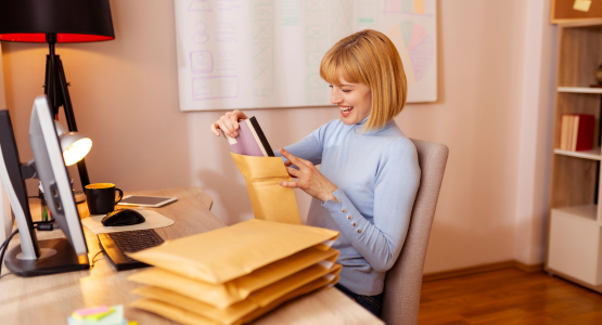 Eine Frau, die am Schreibtisch sitzt und Ware in gepolsterte Versandtaschen verpackt.