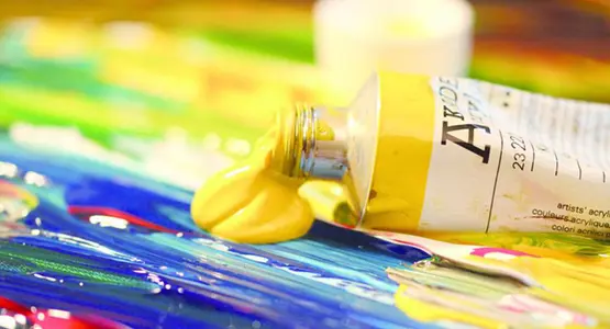 Nahaufnahme einer Tube, aus der gelbe Ölfarbe auf eine Leinwand quillt.