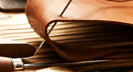 Nahaufnahme einer Nadel, die doppelt durch ein Stück Leder sticht. 