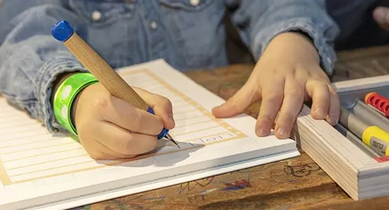 Nahaufnahme eines Kindes, das mit einem Schreiblernfüller in ein Schulheft schreibt.