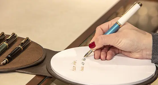 Nahaufnahme einer Hand, die mit Füllfederhalter auf ein Stück Papier schreibt.